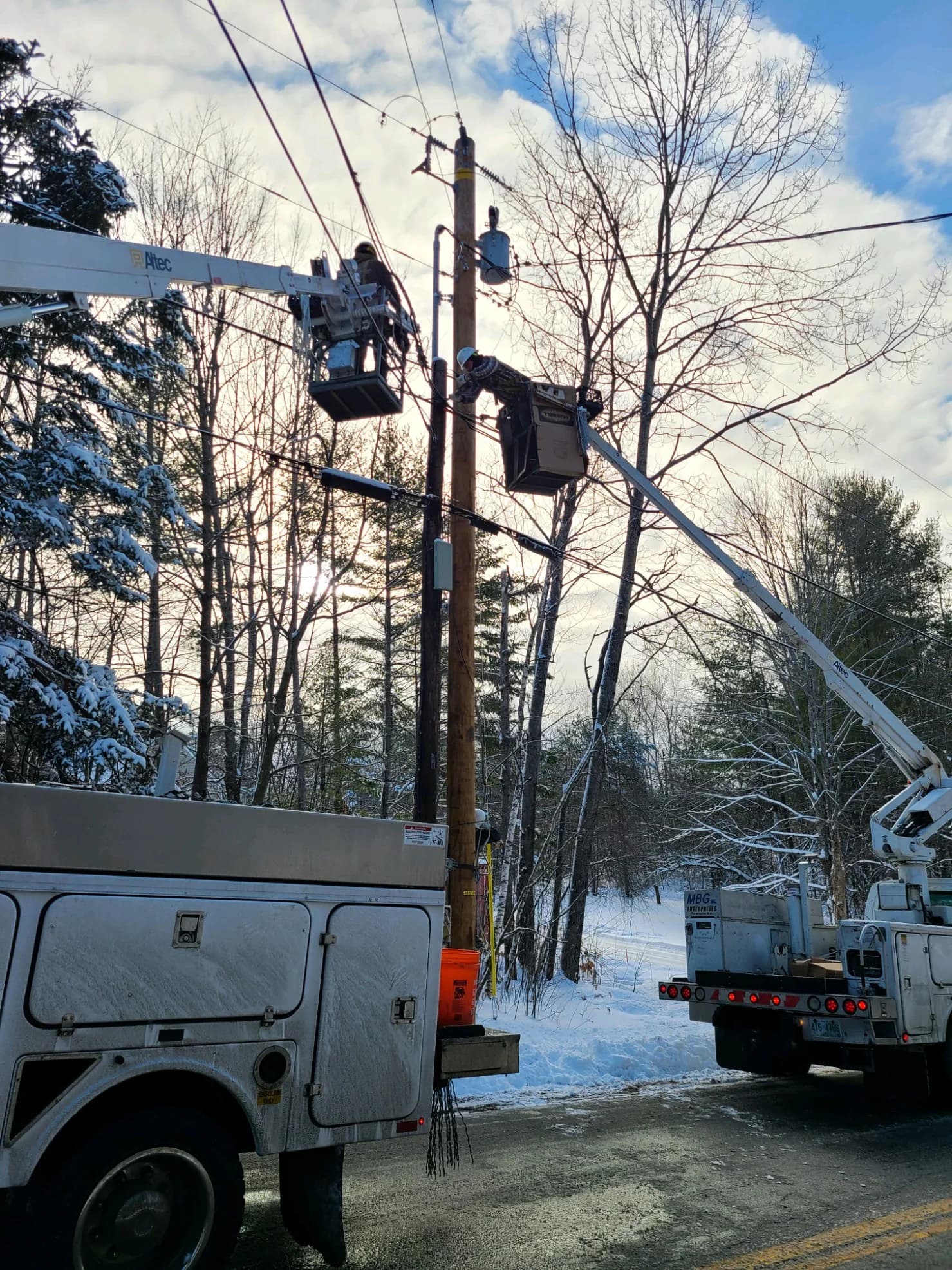 Granite State Utilities bucket crews working aerial cable on a snowy roadside pole line
