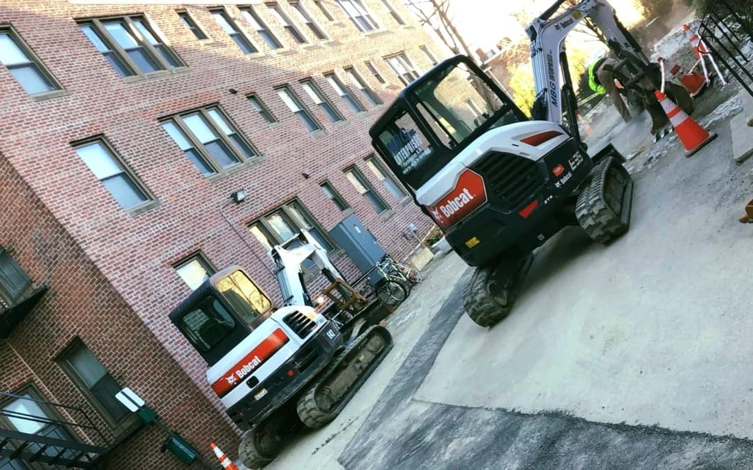 Two MBG Bobcat machines working a tight urban site alongside a brick apartment building