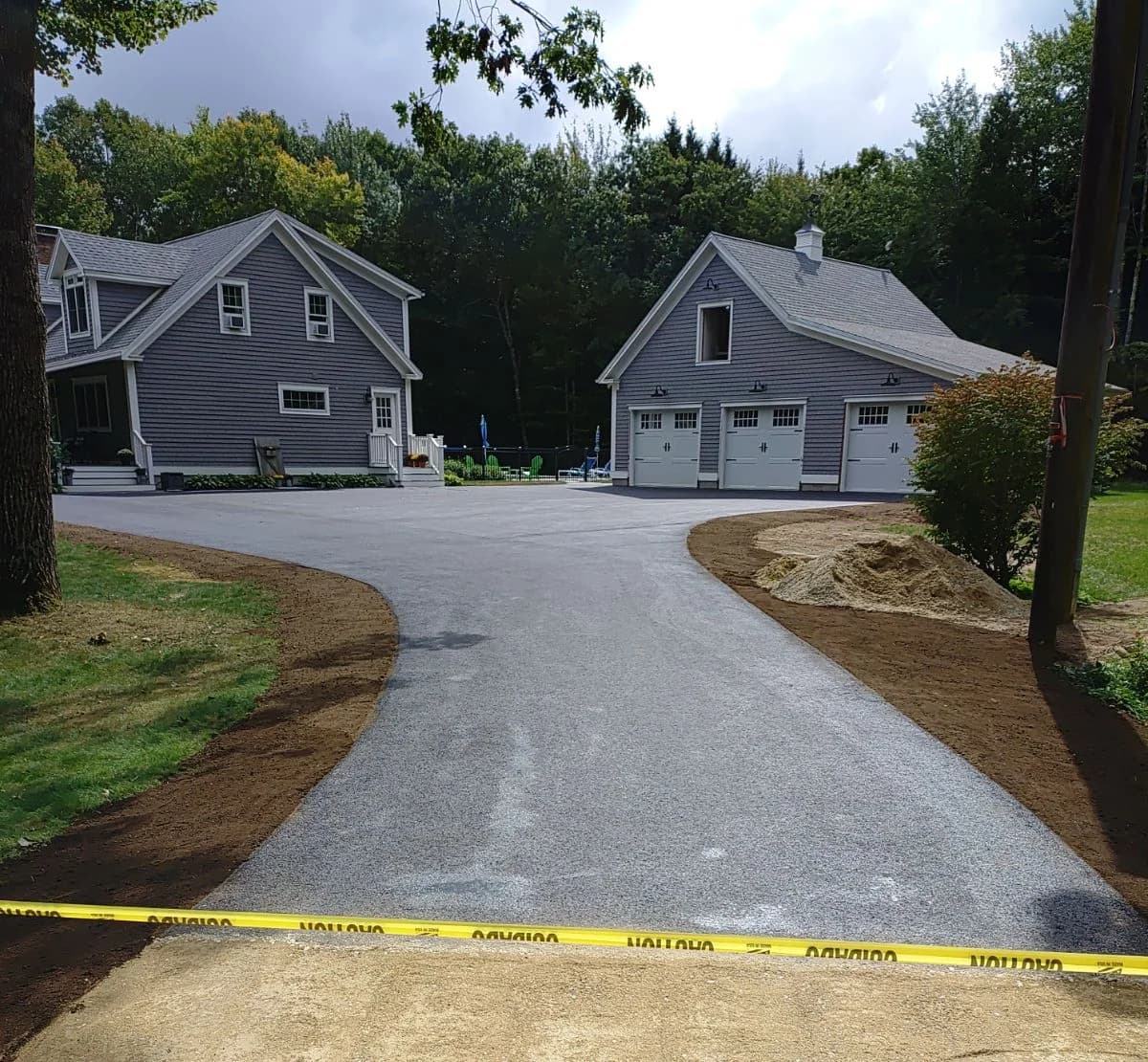 A freshly paved residential driveway curving to a detached three-bay garage
