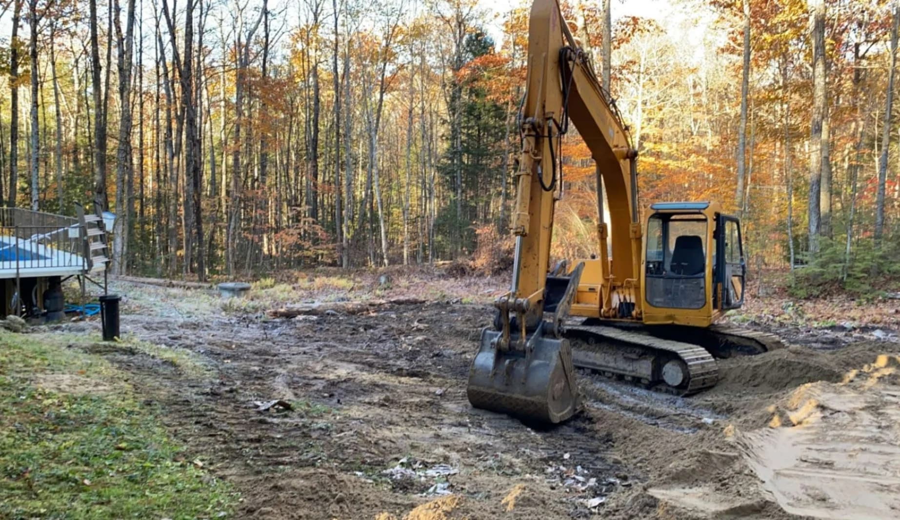 An excavator grading a residential site surrounded by fall foliage