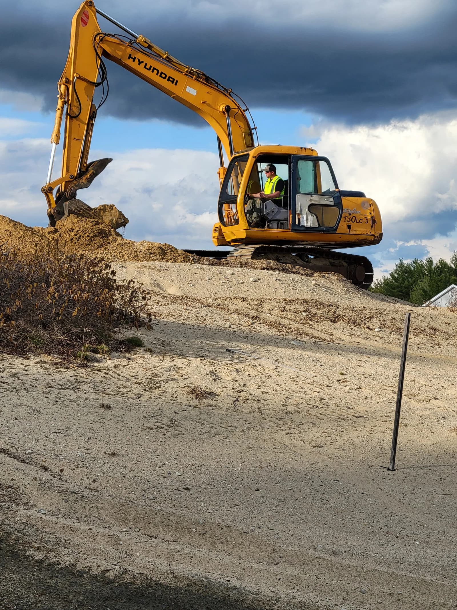 A Hyundai 130LC excavator working a sand and gravel stockpile at golden hour
