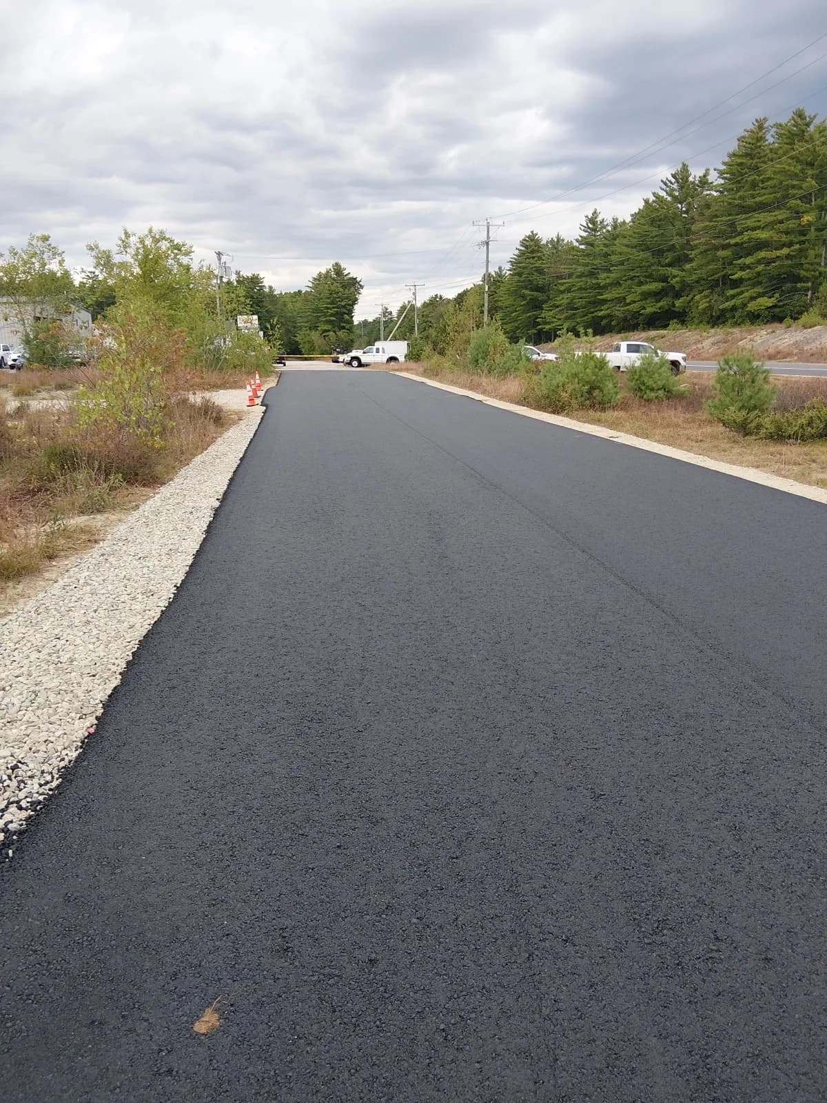 A newly paved commercial access road with a compacted gravel shoulder